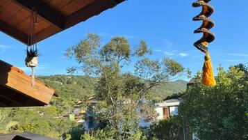 Varanda de madeira com vista para uma paisagem verde e um objeto decorativo pendurado.