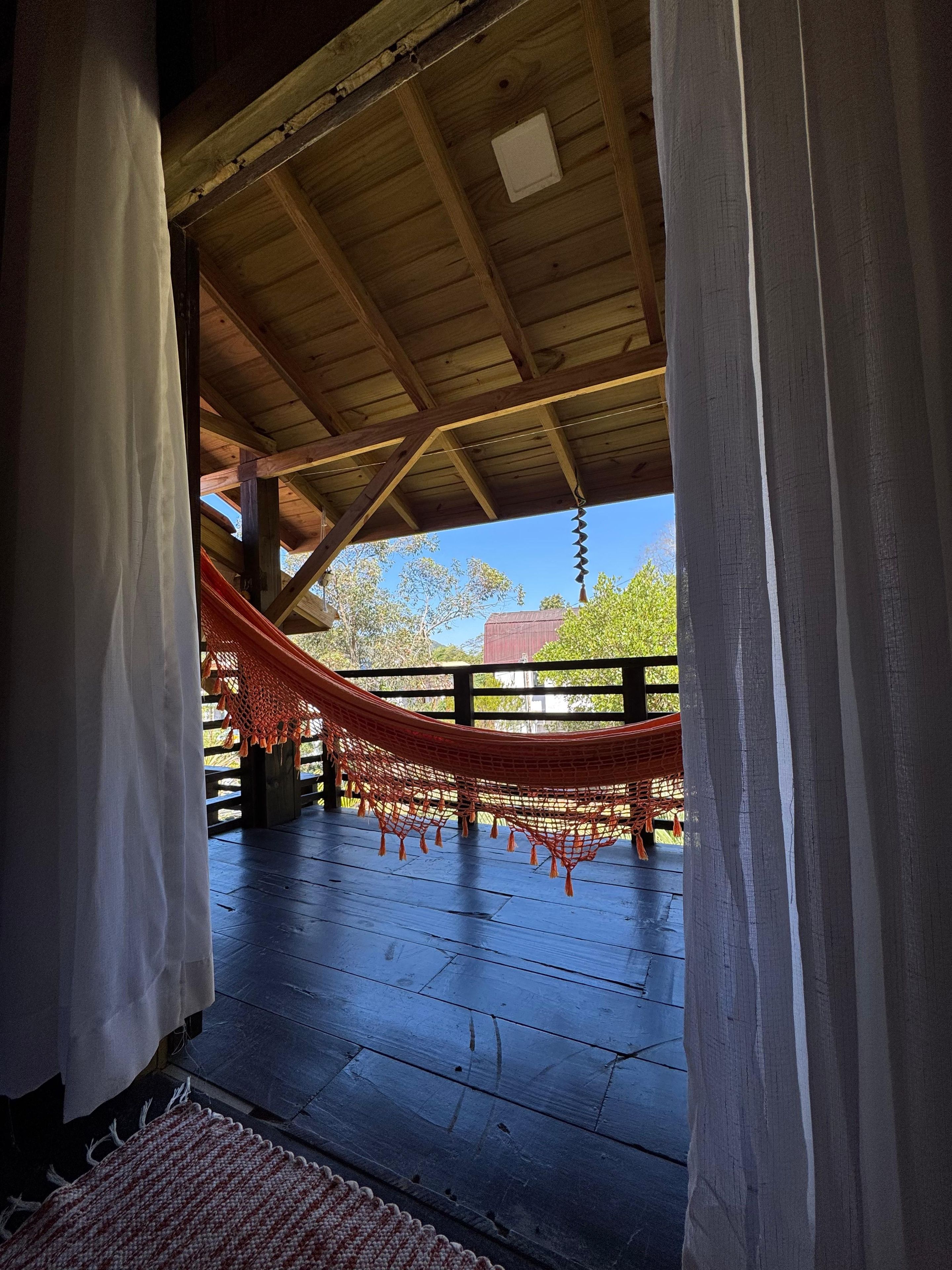 A wooden deck with a hammock and a view of trees and a building in the background.