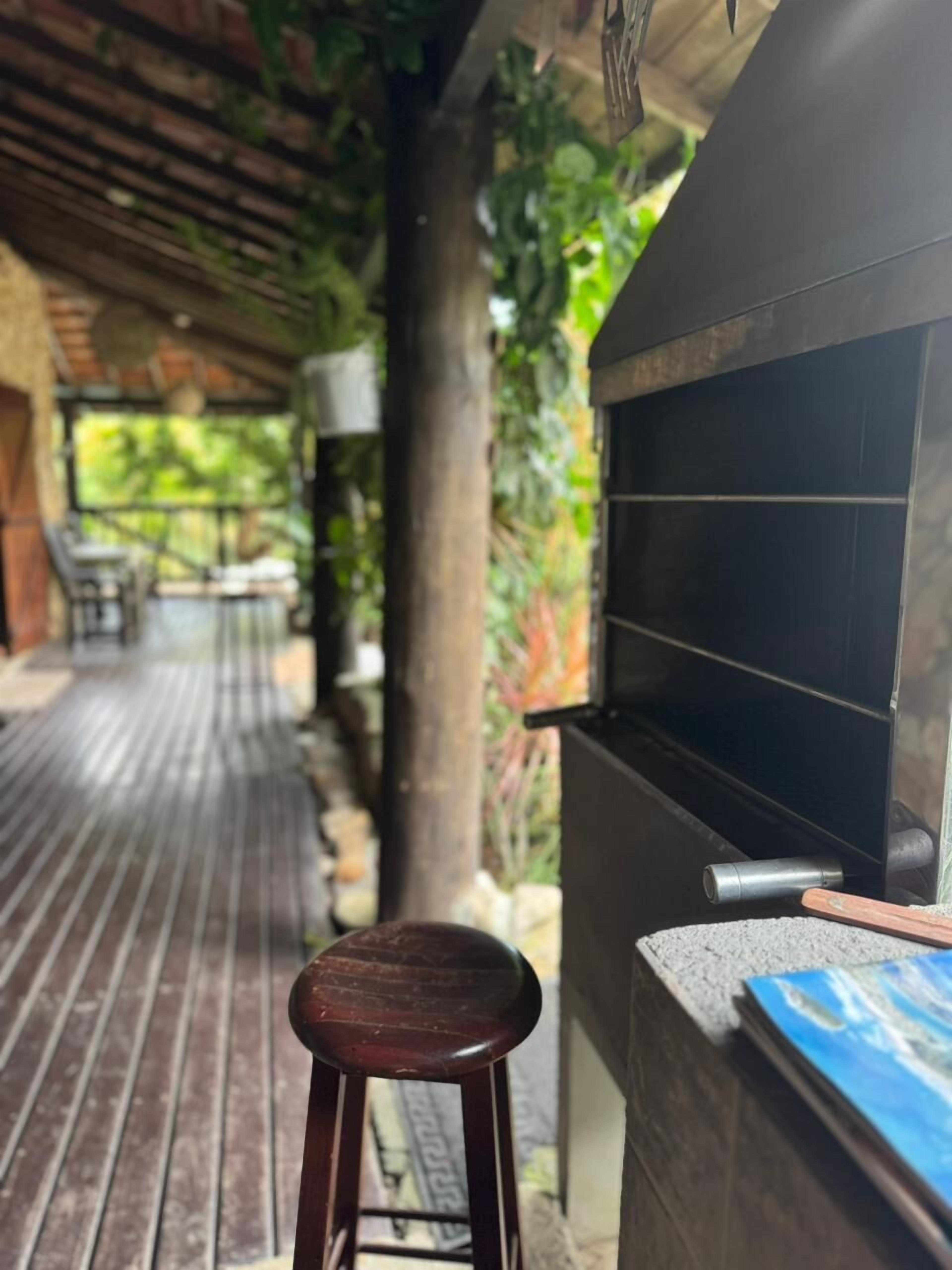 Un espacio al aire libre techado con una parrilla, un banco de madera y una mesa con sillas.