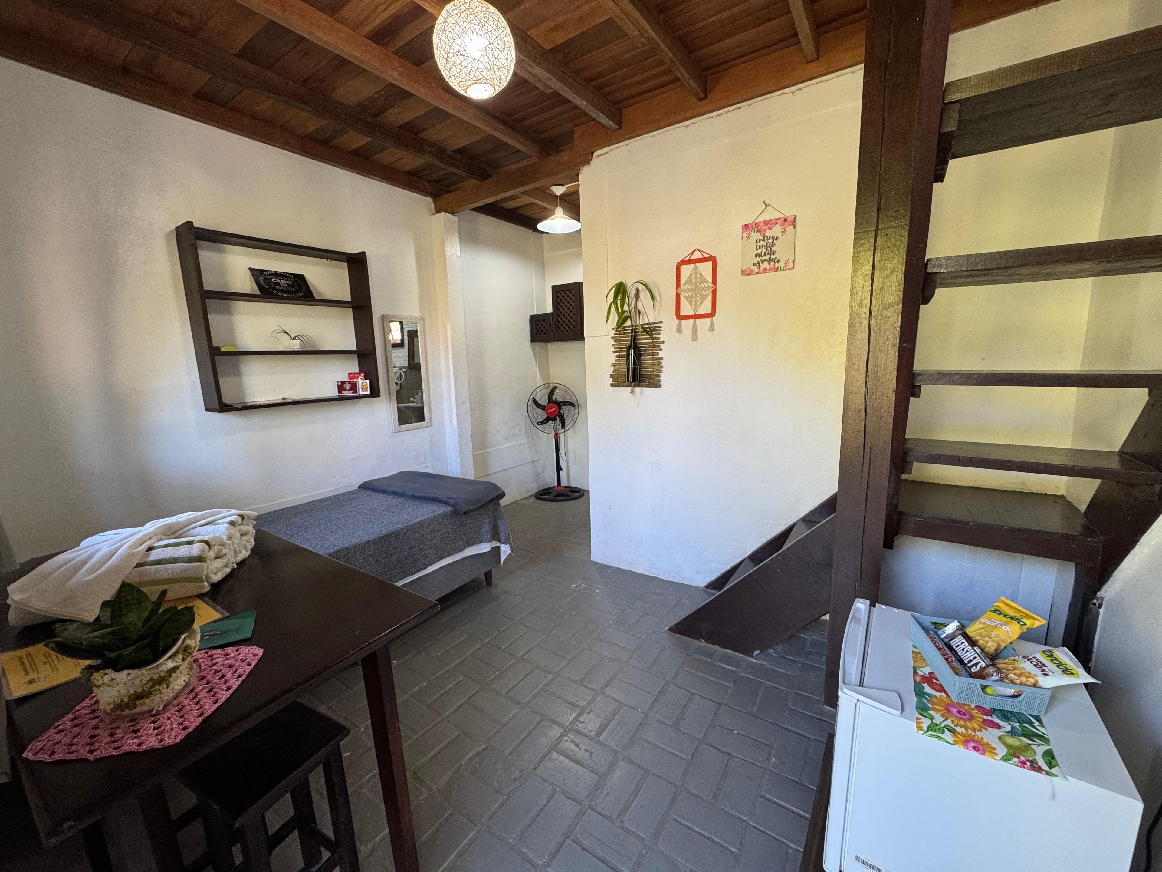 Una habitación con una cama, un escritorio con una planta, un ventilador y una escalera.
