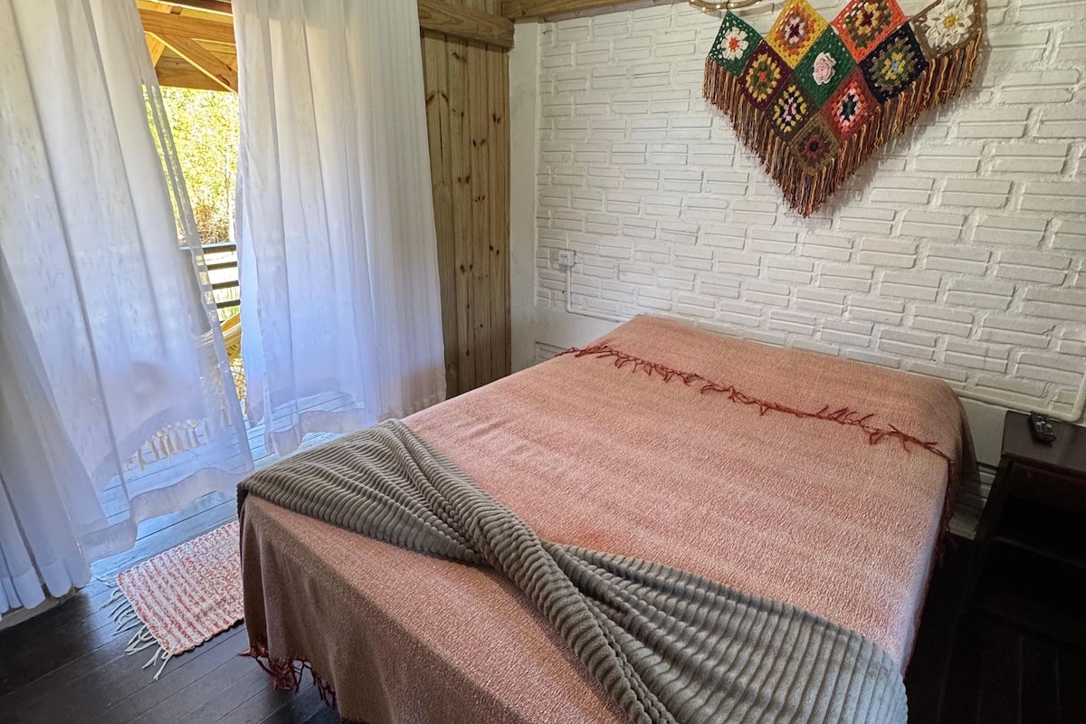 Una habitación con cama, piso de madera, pared de ladrillo blanco y un adorno colgante.