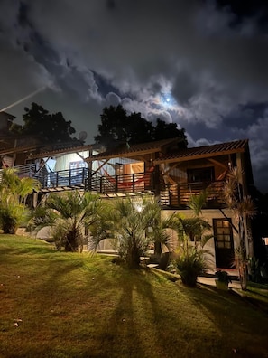 A two-story wooden house with a balcony, surrounded by a well-maintained lawn and palm trees. - Pousada Vale da Praia (Imbituba)