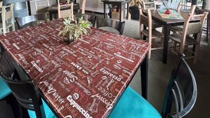 Un'area pranzo con un tavolo ricoperto da una tovaglia rossa con scritte a tema caffè, circondato da sedie.