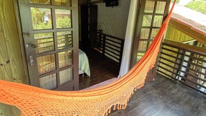 Una casetta di legno con un'amaca, una porta che dà su una stanza con un letto e vista sul verde circostante.