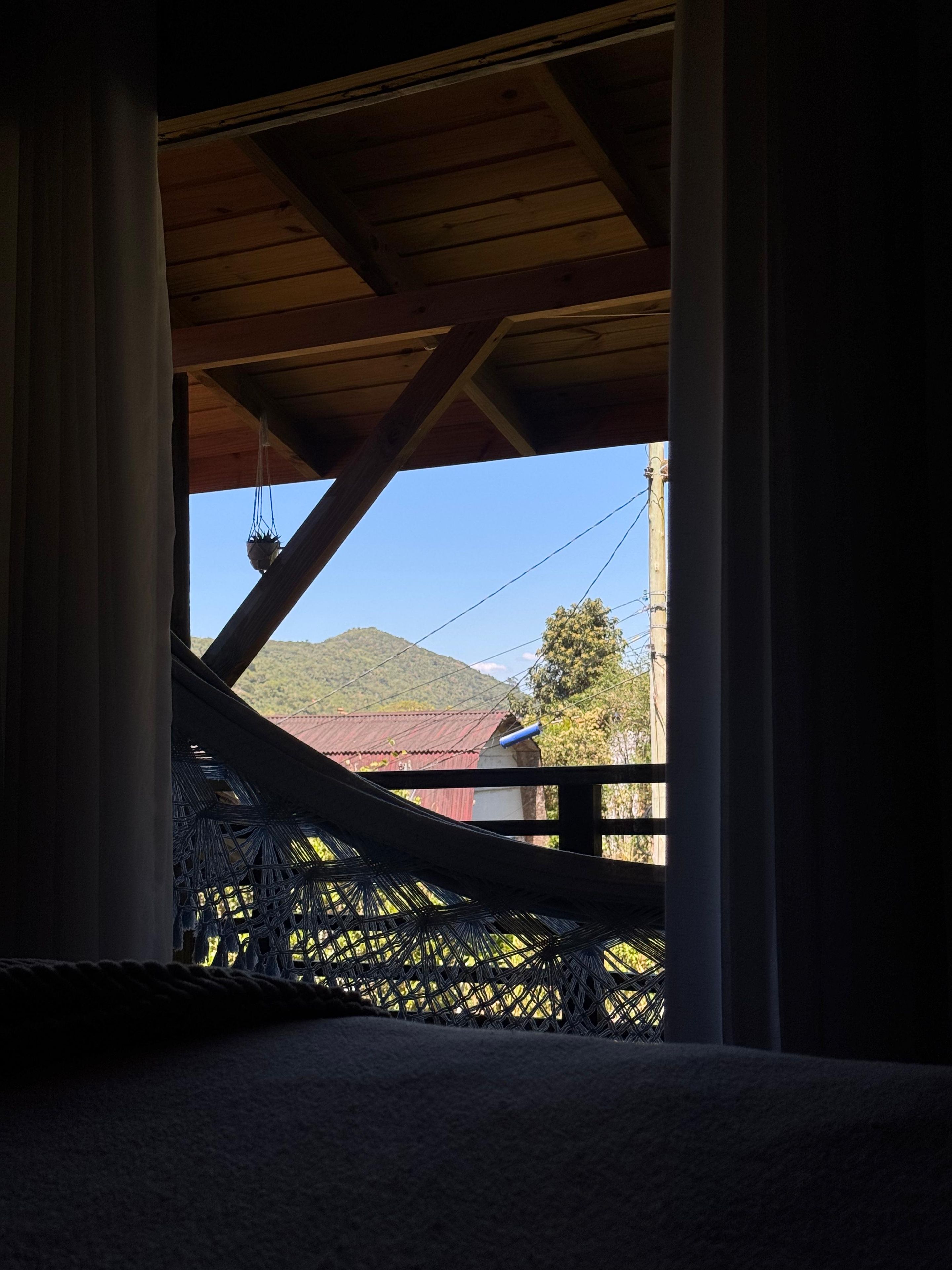 Una hamaca bajo una estructura de madera, con vista a una montaña y un edificio.