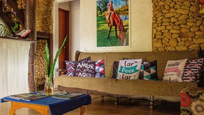 A cozy living room with a wooden bench adorned with colorful pillows, a wooden table with a magazine, and a stone wall in the background.