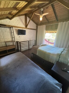 A room with two beds, a TV mounted on the wall, a hammock outside the window, and a ceiling fan. - Pousada Vale da Praia (Imbituba)