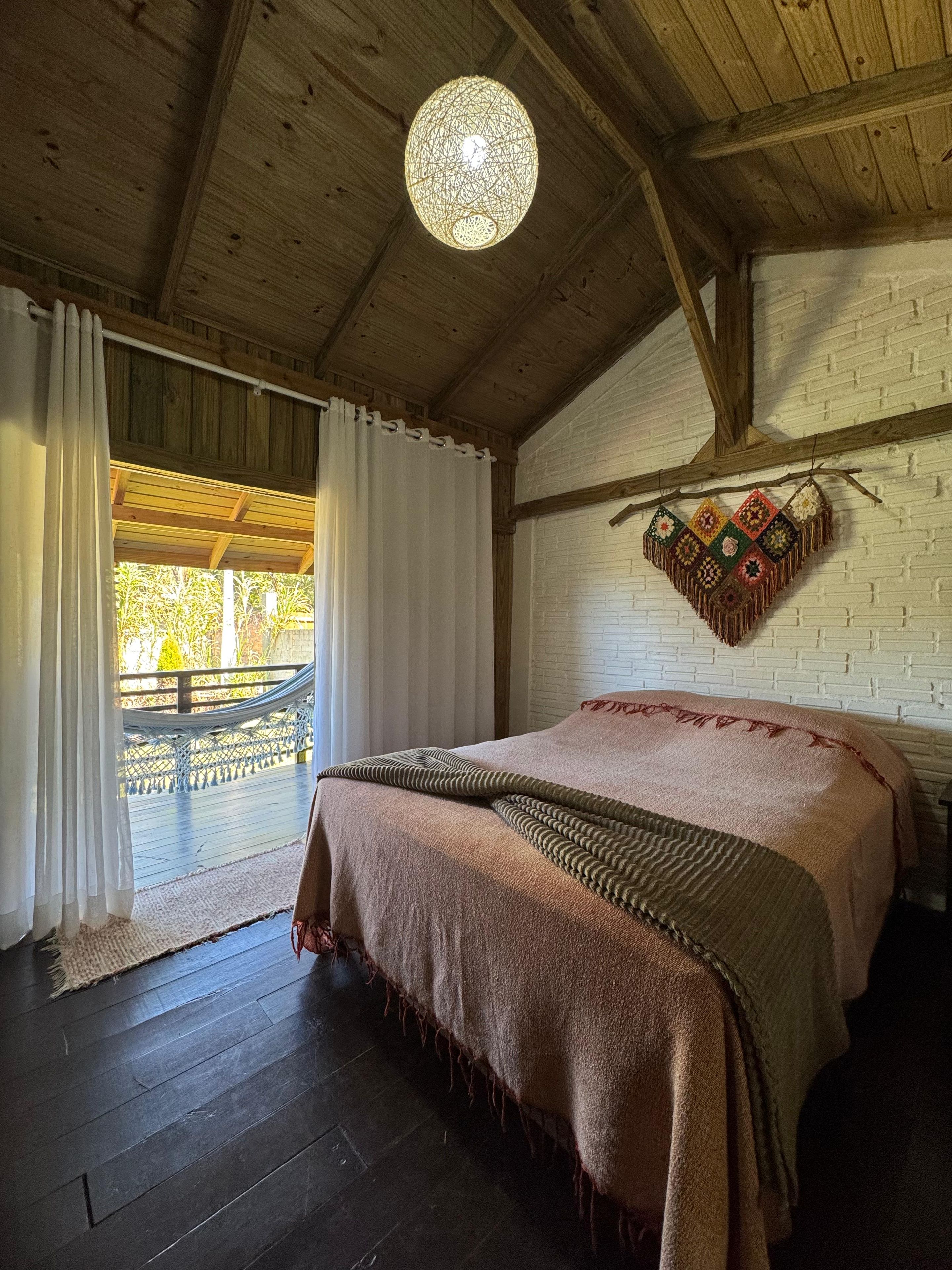 Un dormitorio con techo de madera, una cama con colcha estampada, un colcha colgante y vistas al exterior.