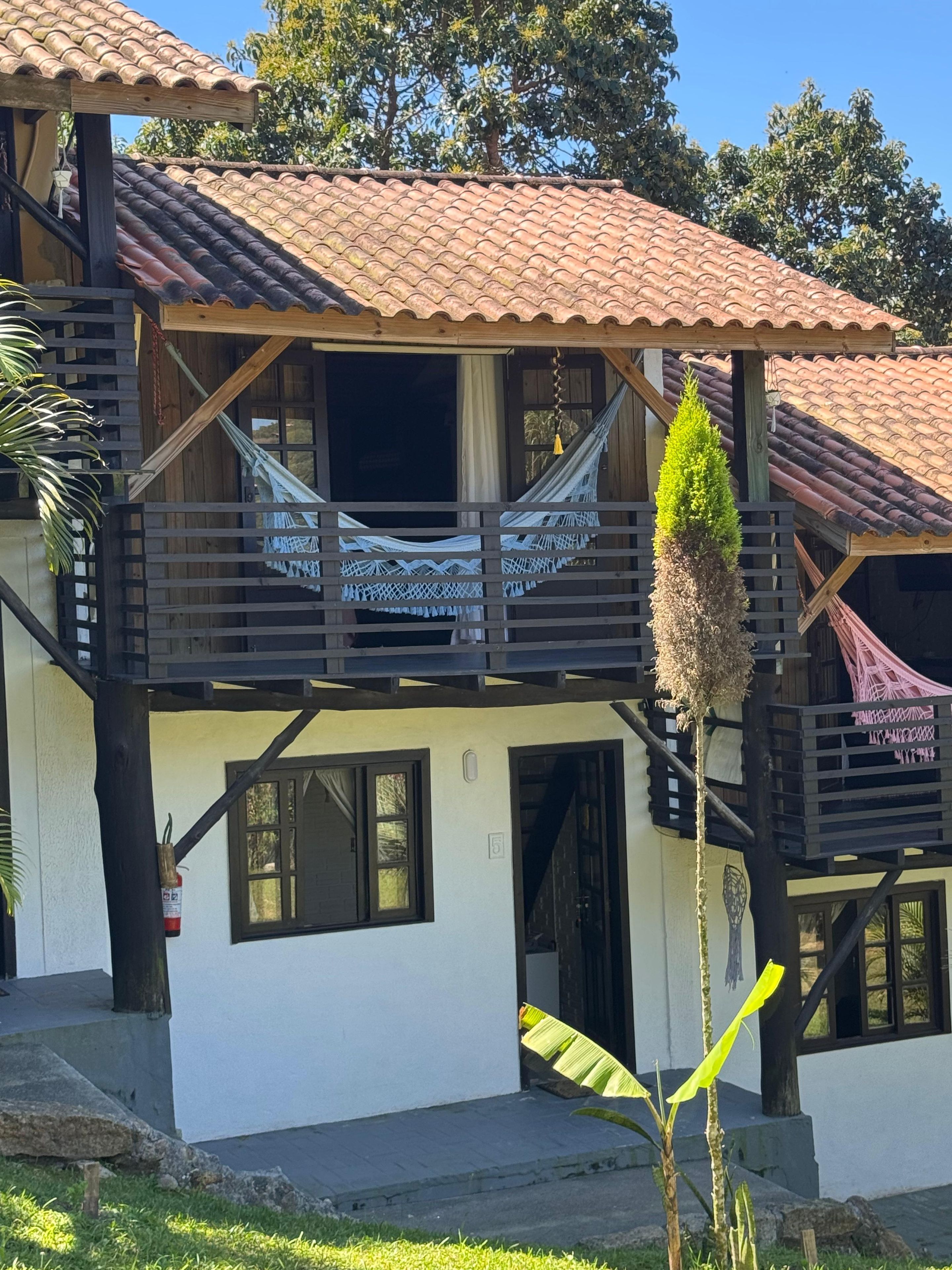 Um edifício de dois andares com varanda, rede e um pequeno jardim.