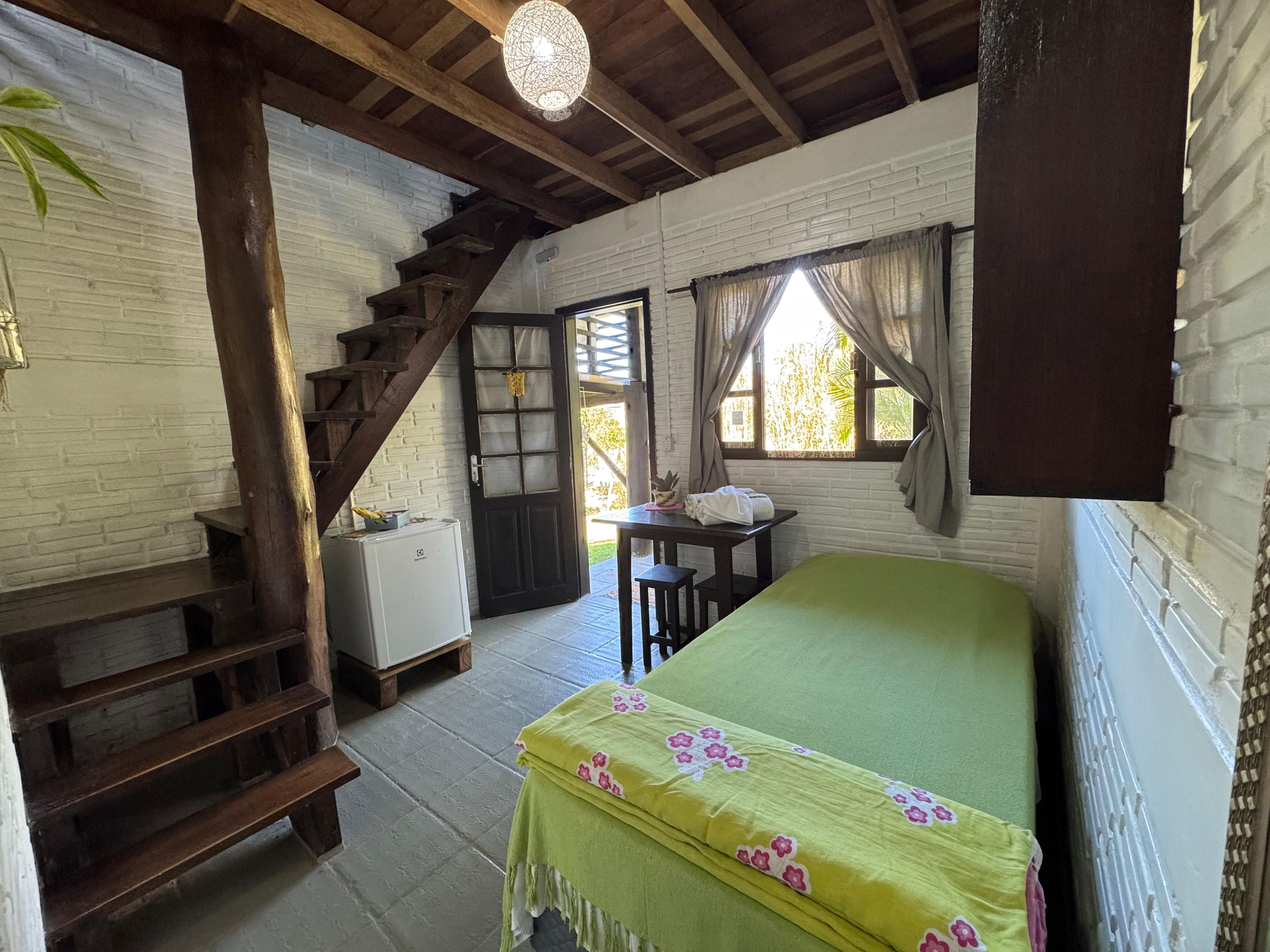Una habitación con una cama, una mesita, una silla, una escalera y una ventana.