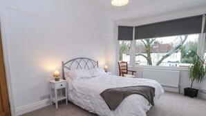 Ein Schlafzimmer mit Bett, Nachttischen, einem Sessel, einem Fenster mit Blick und einer Heizung.
