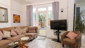 Ein Wohnzimmer mit Sofa, Sessel, Glastisch und Flachbildfernseher.