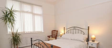 Une chambre bien rangée, avec un lit, des tables de chevet, une chaise et une plante en pot.