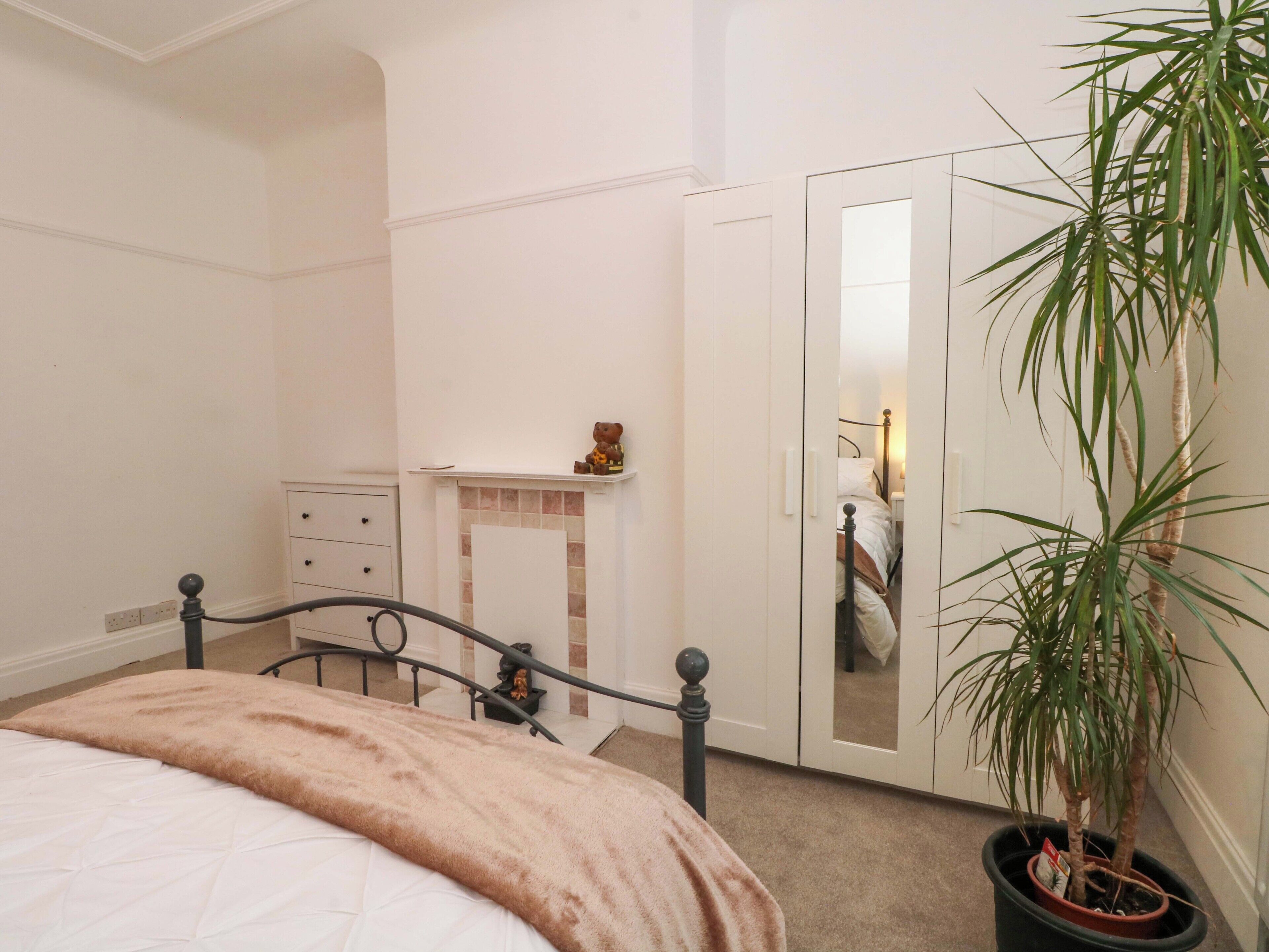 A bedroom with a bed, a dresser, a nightstand, a mirror, and a potted plant.