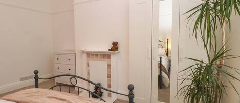 A bedroom with a bed, a dresser, a nightstand, a mirror, and a potted plant.