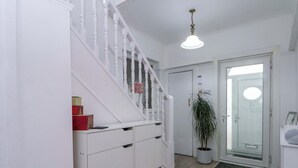Ein Flur mit weißer Treppe, einer Topfpflanze, einer Tür mit Glasfenster und einer Leuchte.