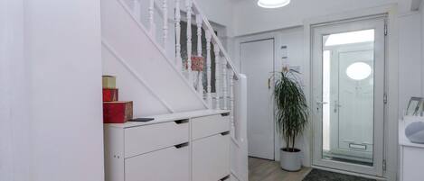 A hallway with a white staircase, a potted plant, a door with a glass panel, and a light fixture.