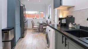 Una cocina compacta con lavadora integrada, un comedor con mesa y sillas, y un ventanal que proporciona luz natural.