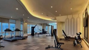 Une salle de sport spacieuse équipée de tapis de course, d’appareils de musculation et d’une grande fenêtre laissant entrer la lumière naturelle.