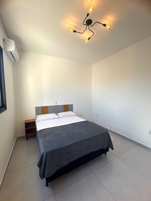 A modern bedroom with a bed, bedside tables, and a unique ceiling light fixture. - Sobrado 03 (Florianópolis)