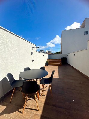 A patio with a round table and four chairs, a small potted plant, and a wooden bench. - Sobrado 03 (Florianópolis)