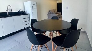 A modern kitchen with white cabinets, a black countertop, and a white refrigerator. There is a round table with black chairs in the center of the room. - Sobrado 03 (Florianópolis)