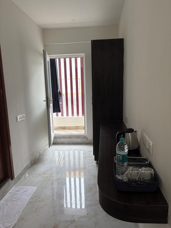 A hallway with a marble floor, a dark-colored cabinet, a water bottle, and a kettle on a counter. - Hotel Elevate Inn Bangalore Airport (Bengaluru)