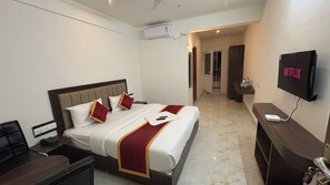 Ein Hotelzimmer mit einem Bett, einem Schreibtisch, einem Sessel, einem Fernseher und einer Wand-Klimaanlage.