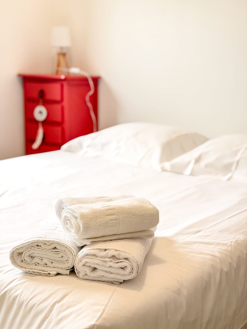 A neatly made bed with white linens and two rolled towels on top.