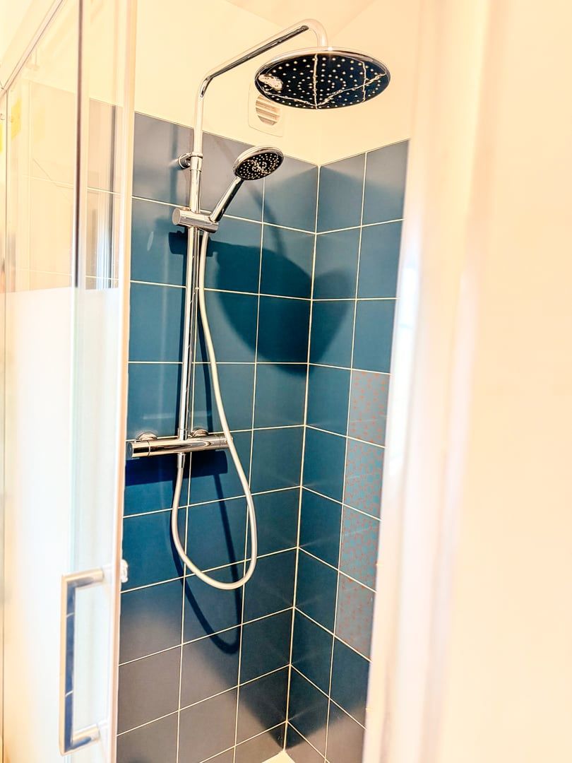 A shower with a handheld showerhead and a fixed overhead showerhead in a bathroom with blue-tiled walls.