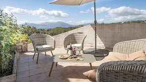 Eine Terrassengaststätte mit Korbmöbeln, einem Tisch mit Speisen und Blick auf Berge.