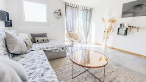 Ein modernes Wohnzimmer mit einer Couch, einem Glastisch und einem großen Fenster mit Vorhängen.