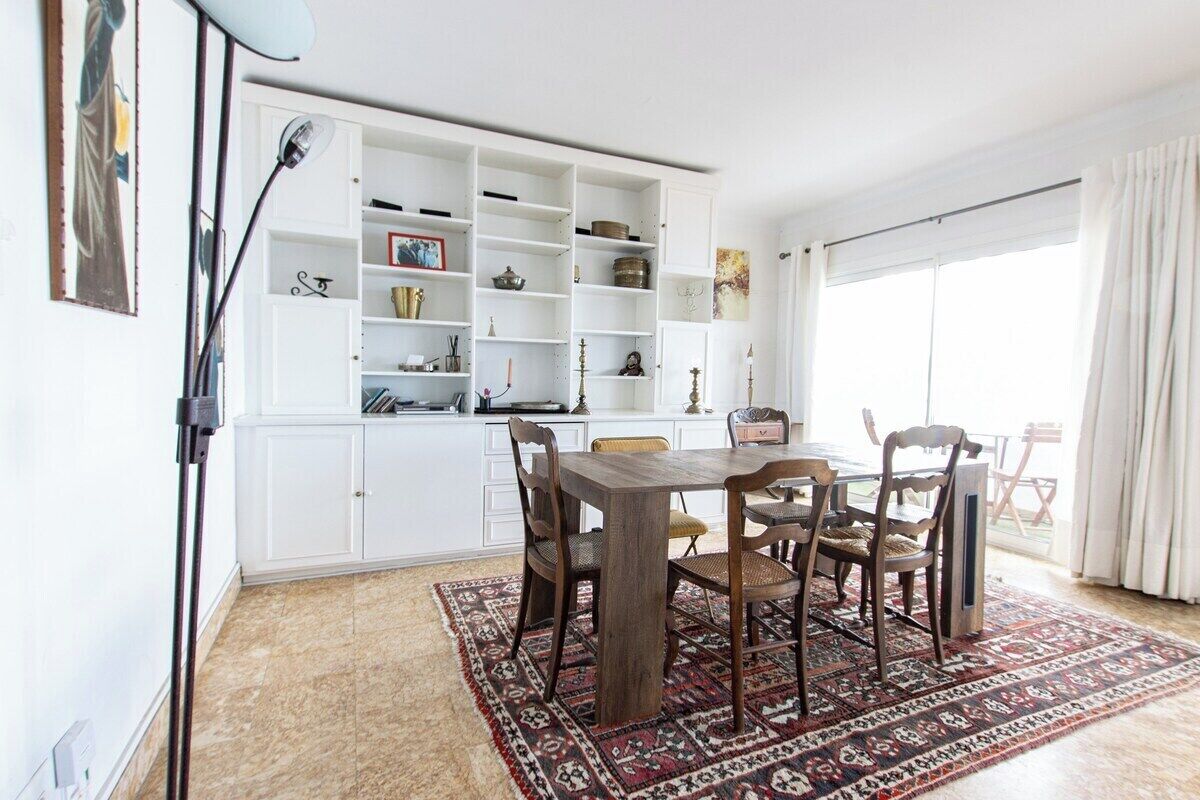 Un comedor con una mesa y sillas de madera, un tapete estampado y un estante empotrado blanco con varios objetos.