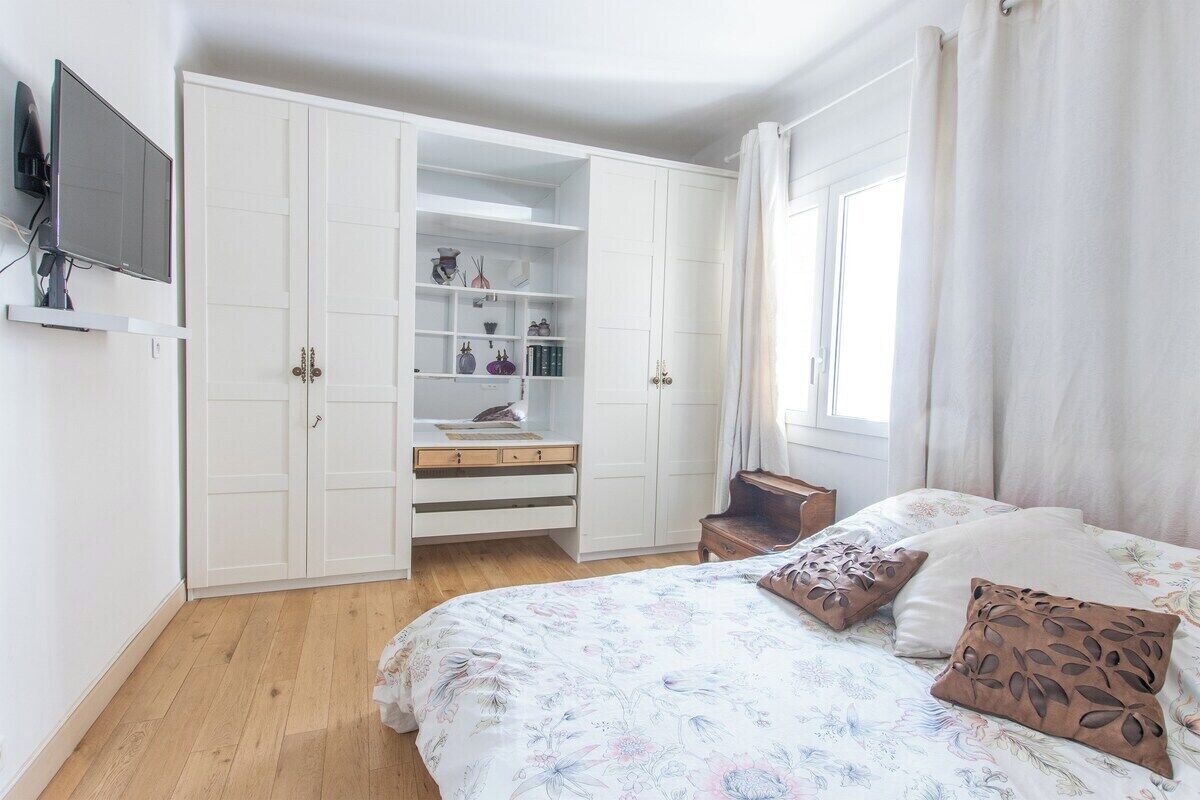 Une chambre à coucher avec un lit, une armoire, une télévision et une fenêtre avec des rideaux.