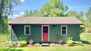 A small, single-story house with a red door, two windows, and a green exterior. - Cozy cottage with local art (Tillson)