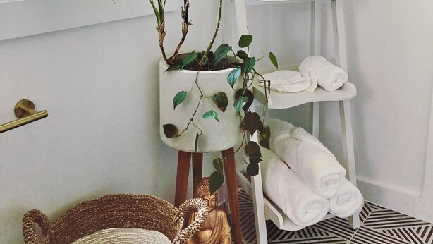 A bathroom with a white vanity, a hanging plant, a Buddha statue, and a patterned floor. - Cozy cottage with local art (Tillson)