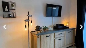 A modern living room with a wooden cabinet, a flat-screen TV mounted on the wall, and a floor lamp with multiple bulbs. - "I Cavadilli" – Peaceful Studio | by Efficios (Propriano)