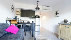 A compact living space with a kitchenette, a sofa with a bright pink pillow, and a dining area with a wooden table. - "I Cavadilli" – Peaceful Studio | by Efficios (Propriano)