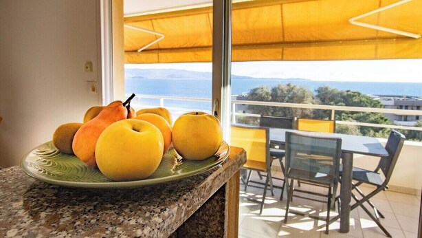 A kitchen counter with a plate of fruit and a view of a balcony with outdoor furniture. - "I Sanguinari" – 2BR Sea View Apt | by Efficios (Ajaccio)
