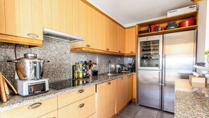 A kitchen with wooden cabinets, granite countertops, a built-in oven, and a stainless steel refrigerator. - "I Sanguinari" – 2BR Sea View Apt | by Efficios (Ajaccio)