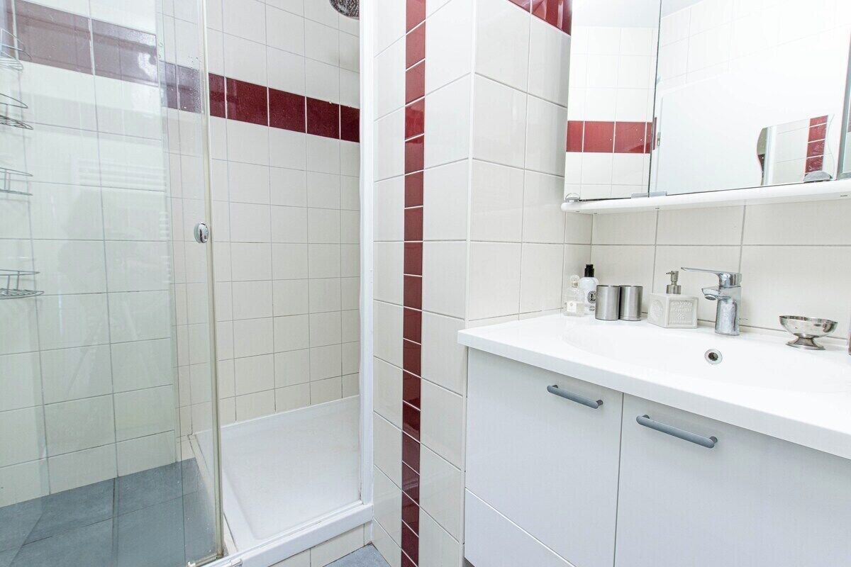 A bathroom with white tiles, a glass shower enclosure, and a white countertop with toiletries.