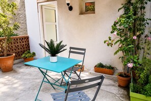 A patio with a turquoise table and two chairs, a potted plant, and a wall-mounted light fixture. - "U Roccapina" – Downtown Studio | by Efficios (Sartène)