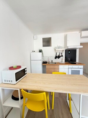A compact kitchen with a microwave, sink, and cabinets. There is a wooden table with yellow chairs. - "U Roccapina" – Downtown Studio | by Efficios (Sartène)