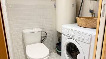 Ein kleines Badezimmer mit Toilette, Waschmaschine und Warmwasserbereiter.