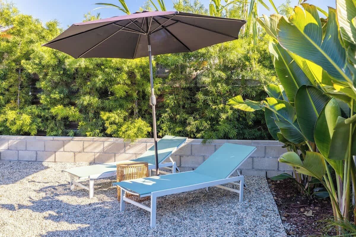 Un espace extérieur aménagé avec une table et des chaises, un grand parasol et un décor luxuriant de verdure.