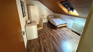 A bedroom with a sloped ceiling, wooden flooring, a bed, a nightstand, a wardrobe, and a skylight. - Apartment for up to 4 people | Kitchen & bathroom | Pension NH (Osterholz-Scharmbeck)