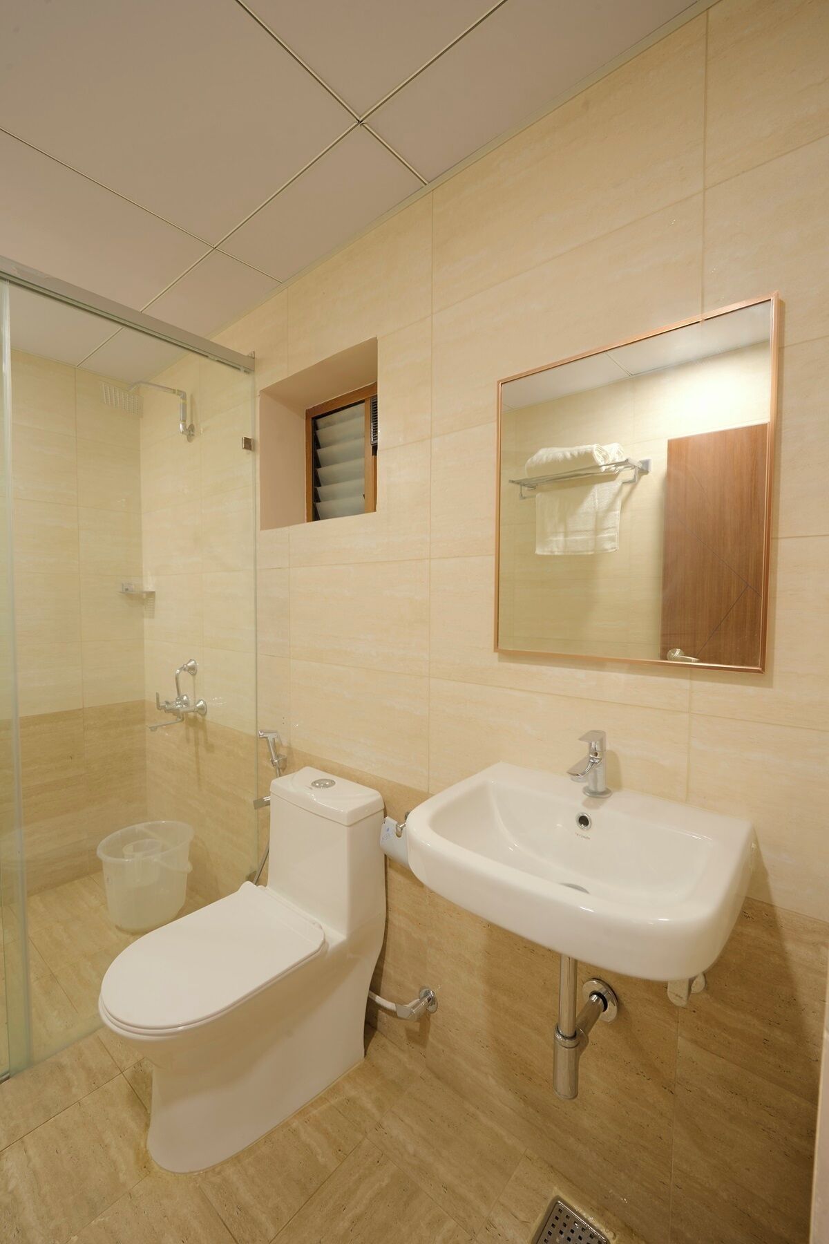Un baño moderno con ducha de vidrio, inodoro y lavamanos con espejo arriba.