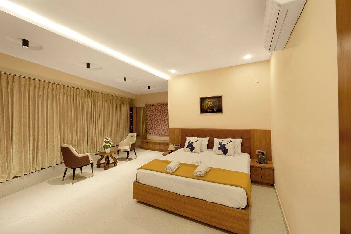 A hotel room with a large bed, a desk, two chairs, and a small table with a flower vase.