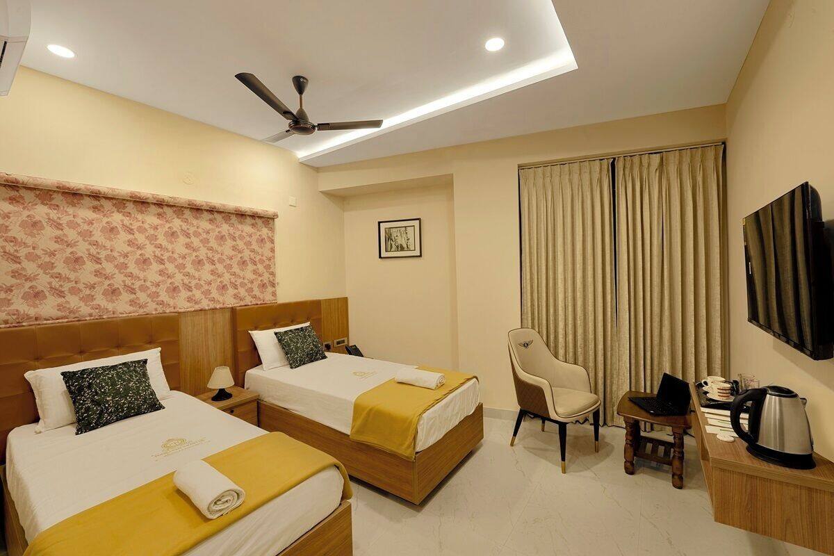 A hotel room with two beds, a desk with a laptop, a chair, a television, and a ceiling fan.