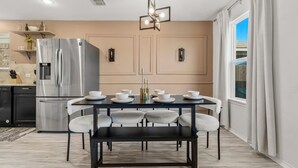 Een moderne keuken met een roestvrijstalen koelkast, een eettafel met stoelen en een kroonluchter.